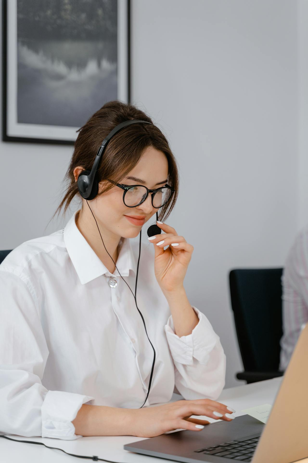 Focused phone agent – A woman in a white shirt and headset works at a laptop, holding the mic near her mouth.