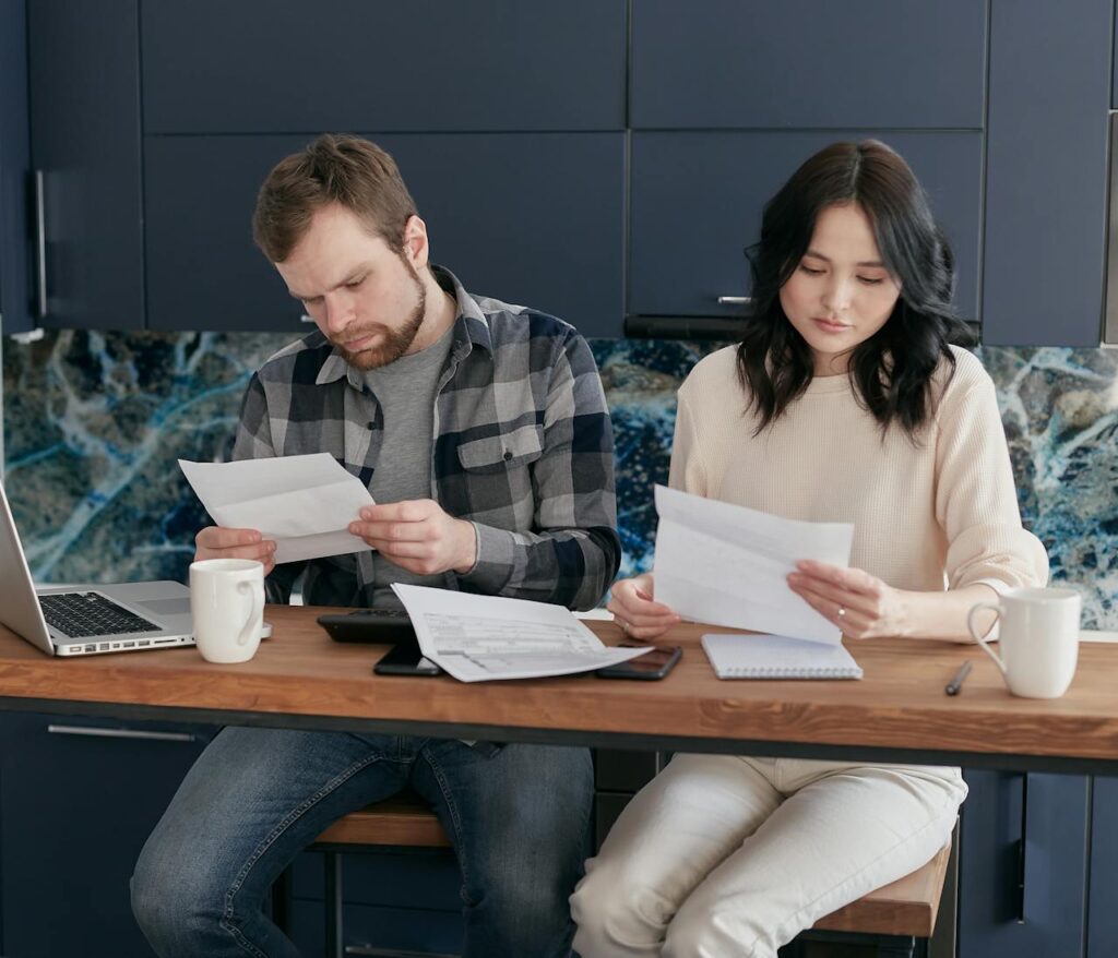 Couple at a table review paperwork with a laptop and coffee mugs.