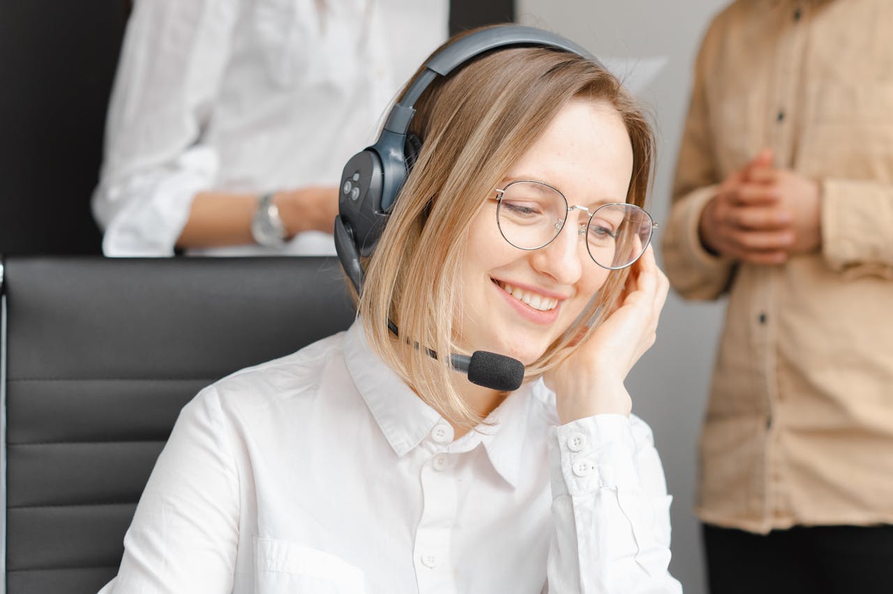 Smiling support agent – Close-up of a headset-wearing woman in a white blouse, smiling as she listens.