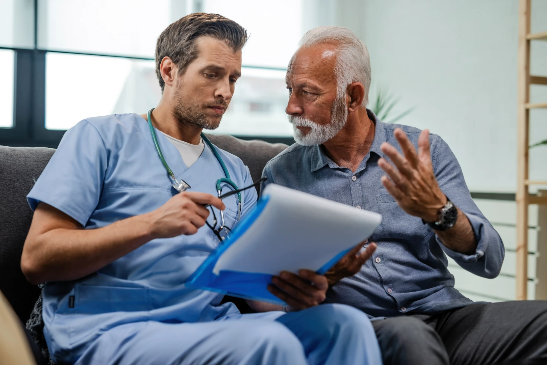 Senior man talking doctor who is reading medical test results while being home visit
